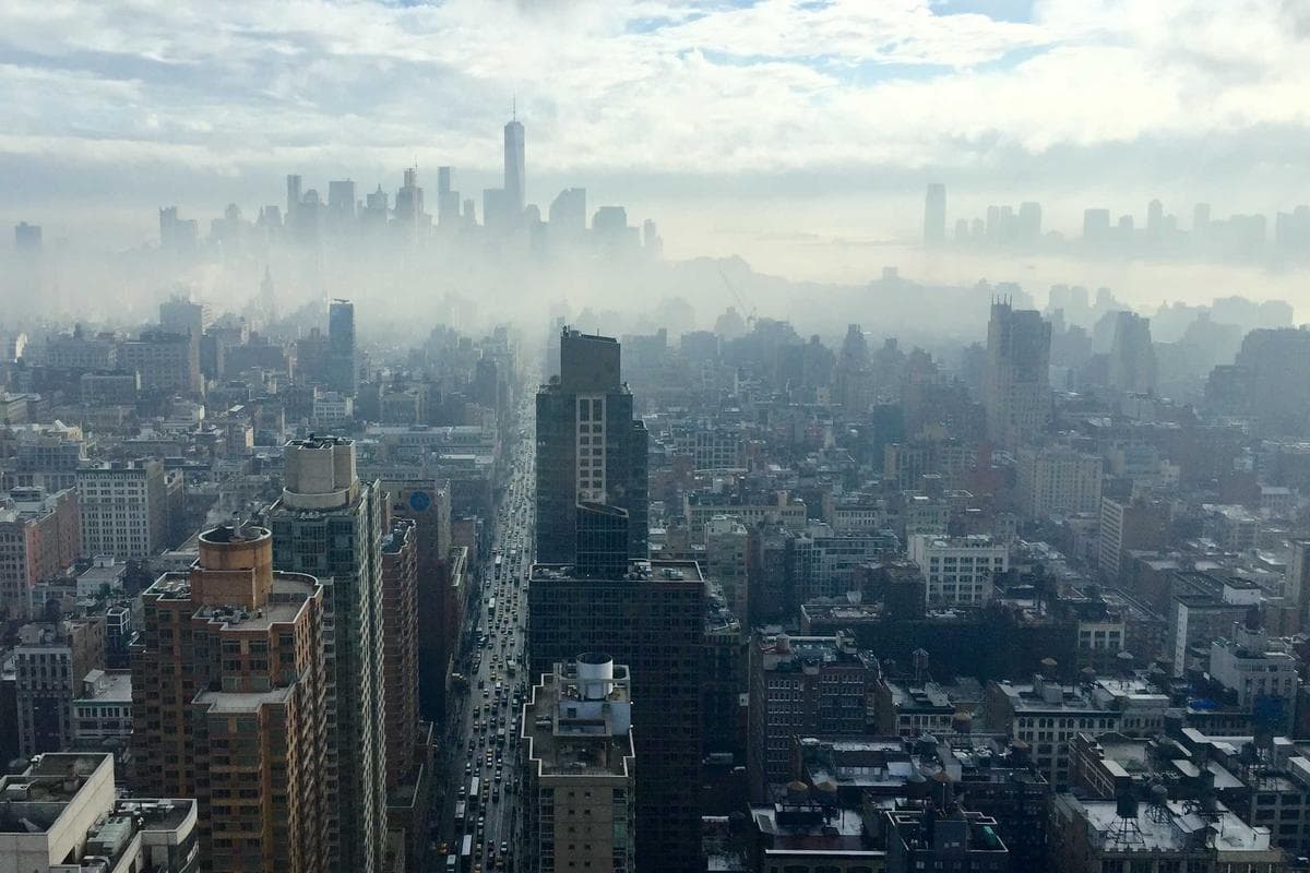 Hoogperspectief op dichtbebouwde straten van New York met hoge wolkenkrabbers gehuld in een dikke mistlaag.