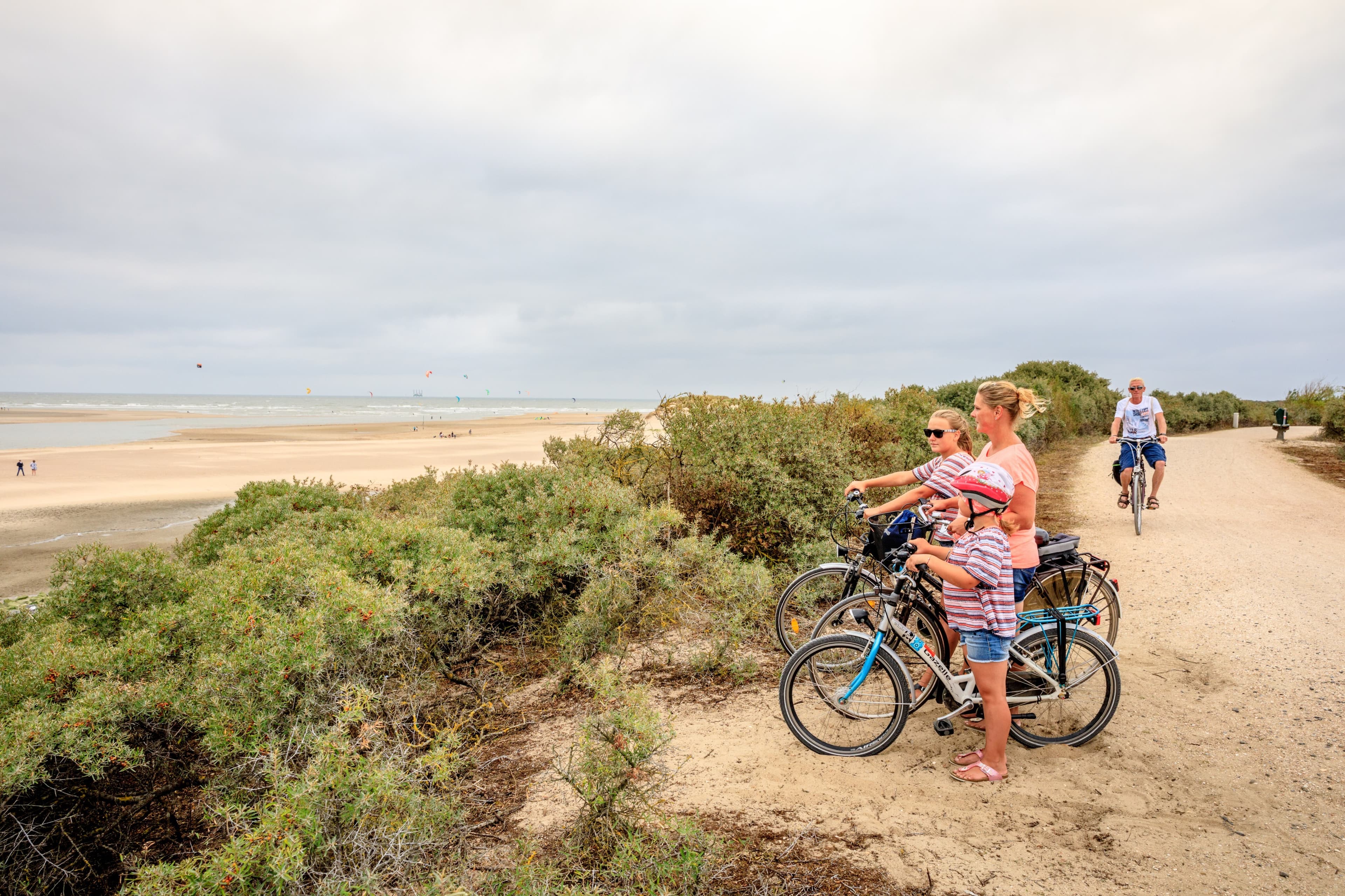 Moeder en twee kinderen op de fiets kijken uit over het duinlandschap met strand en zee op de achtergrond