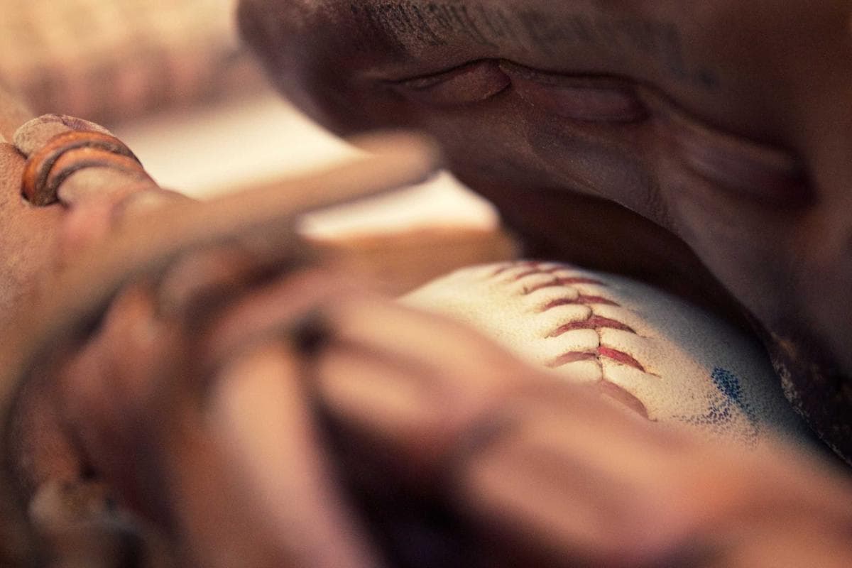 Close-up van een wit honkbal met rode stiksels die stevig in een bruine leren honkbalhandschoen gevangen zit.