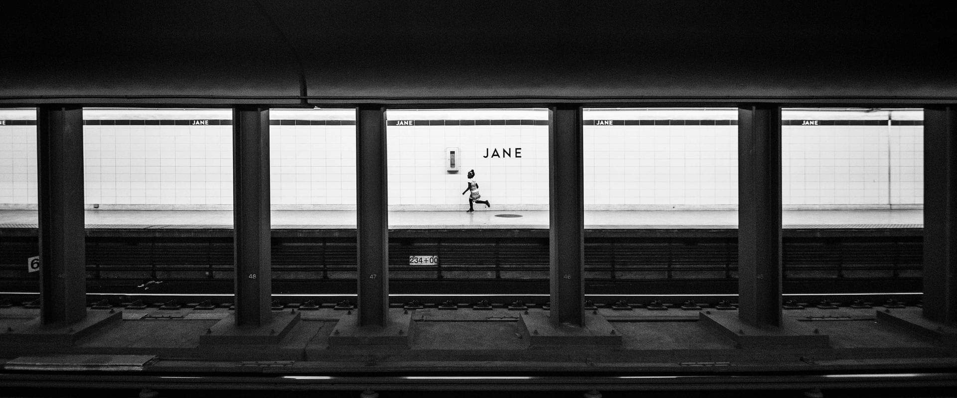 Een jong kind rent over het perron van een metrostation bij de muur met het opschrift JANE.